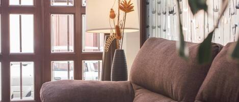 Una sala de estar moderna con un ventanal grande, un sofá y un jarrón decorativo con flores secas.