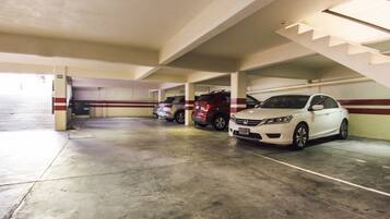 Um estacionamento de vários níveis, com pisos e paredes de concreto, mostrando vários carros estacionados e uma escada que leva a um andar superior.