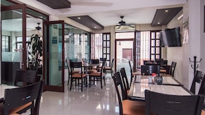 A modern dining area with glass partitions, black chairs, and a flat-screen TV mounted on the wall.