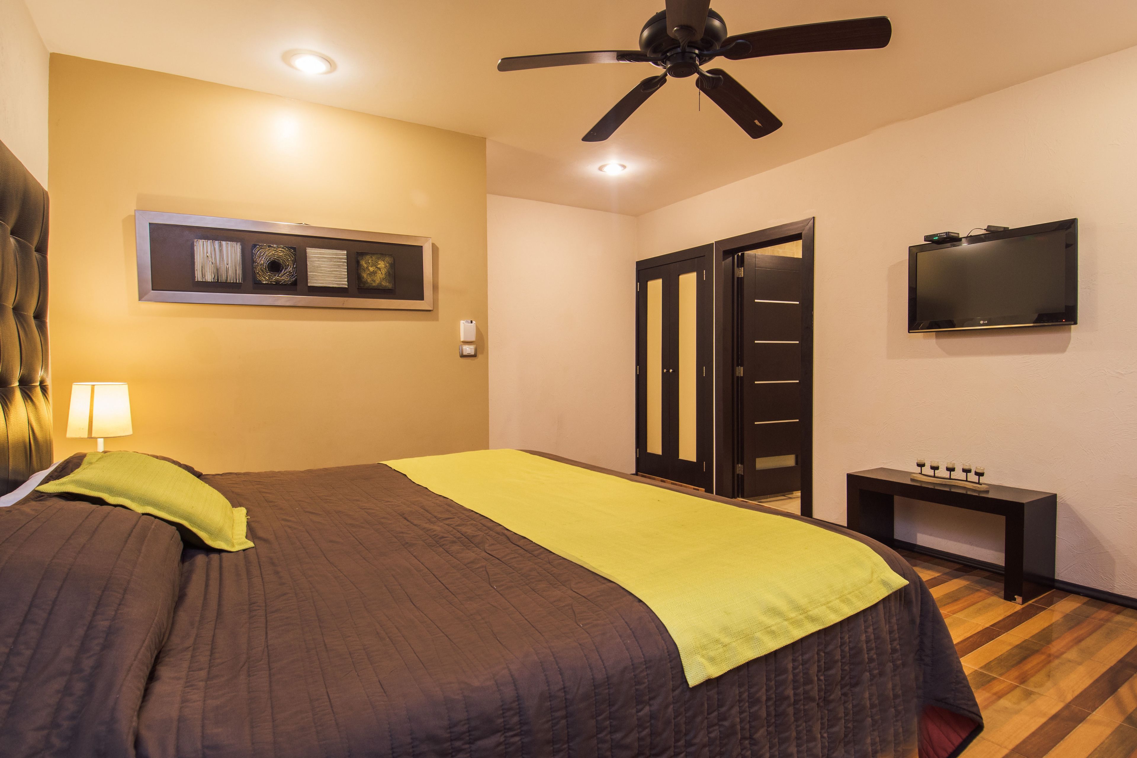 Una habitación de hotel con una cama, ventilador de techo, televisión y una pequeña mesa.