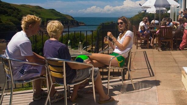A terrace with metal chairs and tables, overlooking a coastal view with hills and the sea. - The Sun Bay Hotel & Restaurant (Kingsbridge)