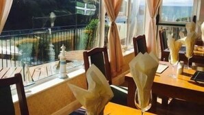 A dining area with tables set for two, featuring a view of a mountainous landscape through large windows. - The Sun Bay Hotel & Restaurant (Kingsbridge)