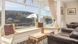 A room with a large window offering a view of a rural landscape, a sofa, a small table, and a radiator. - The Sun Bay Hotel & Restaurant (Kingsbridge)