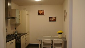 Une cuisine compacte équipée d’une cuisinière, d’un four et de meubles blancs. On y trouve une petite table à manger avec deux chaises et un vase rempli de fleurs jaunes.