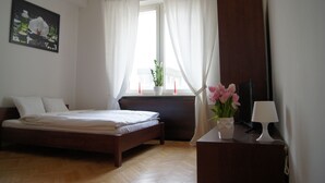 Une chambre à coucher avec un lit, une fenêtre avec des rideaux, une plante, une lampe et un tableau au mur.