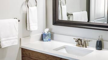 A bathroom with a white sink, two faucets, a mirror, and two towels hanging on towel rings.