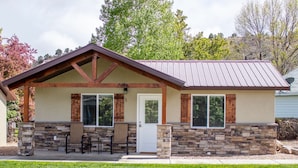 A single-story house with a stone foundation, a gabled roof, and a front porch with two chairs. - Bybee's Steppingstone Motel (Tropic)