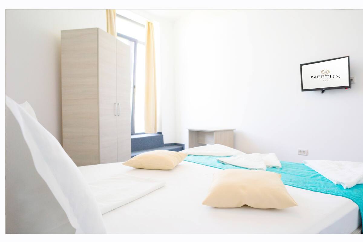 Una habitación de hotel con cama, almohadas, un armario, una mesita de noche y un cartel en la pared.