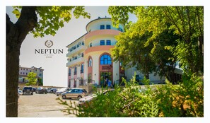 Ein mehrstöckiges Hotel mit geschwungener Fassade, einem markanten Eingangsbereich und einem Parkplatz davor.