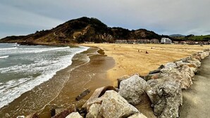 Una playa con un rompeolas rocoso, una orilla arenosa y una colina al fondo.