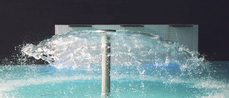 A water feature with a central column and water jets, set against a tiled wall.