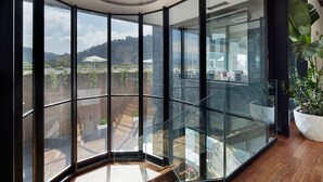 Un interior moderno con amplios ventanales que ofrecen vista a un jardín ajardinado y colinas lejanas.