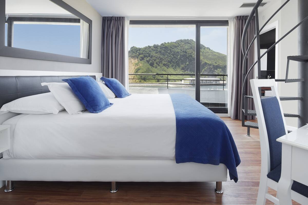 Habitación de hotel moderna con una cama grande, un escritorio y un balcón con vistas panorámicas.