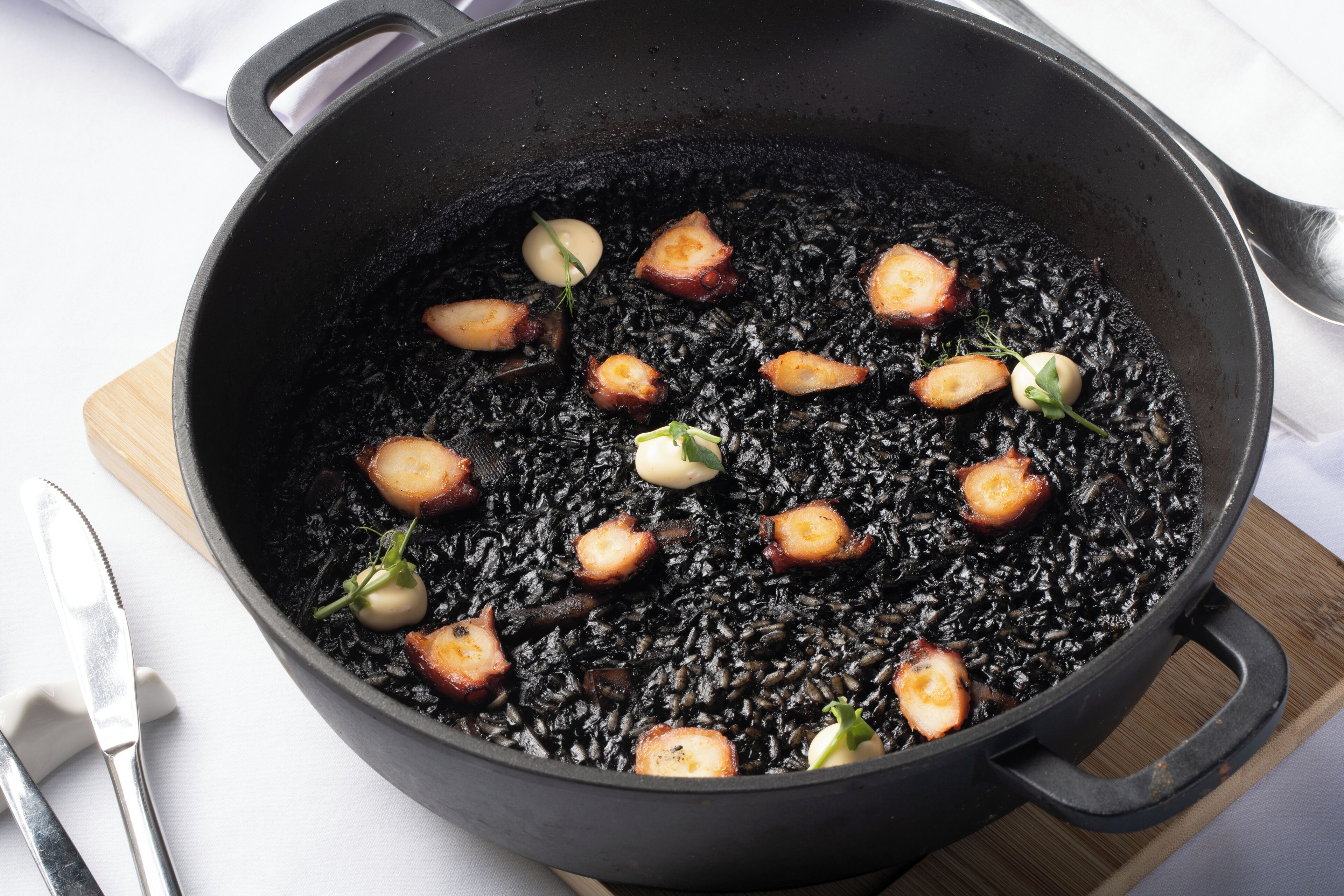 A black skillet with pieces of food, possibly a dish with black rice and meat, on a wooden board.