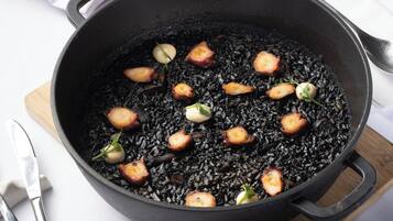 Una sartén negra con trozos de comida, posiblemente un plato de arroz negro y carne, sobre una tabla de madera.
