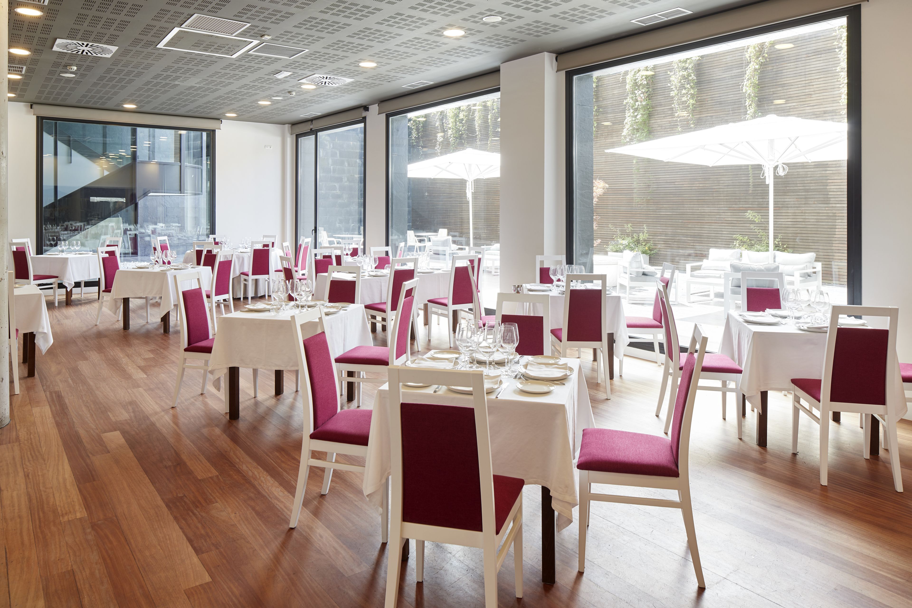 Een restaurant met meerdere tafels en stoelen, grote ramen en binnenshuis planten.