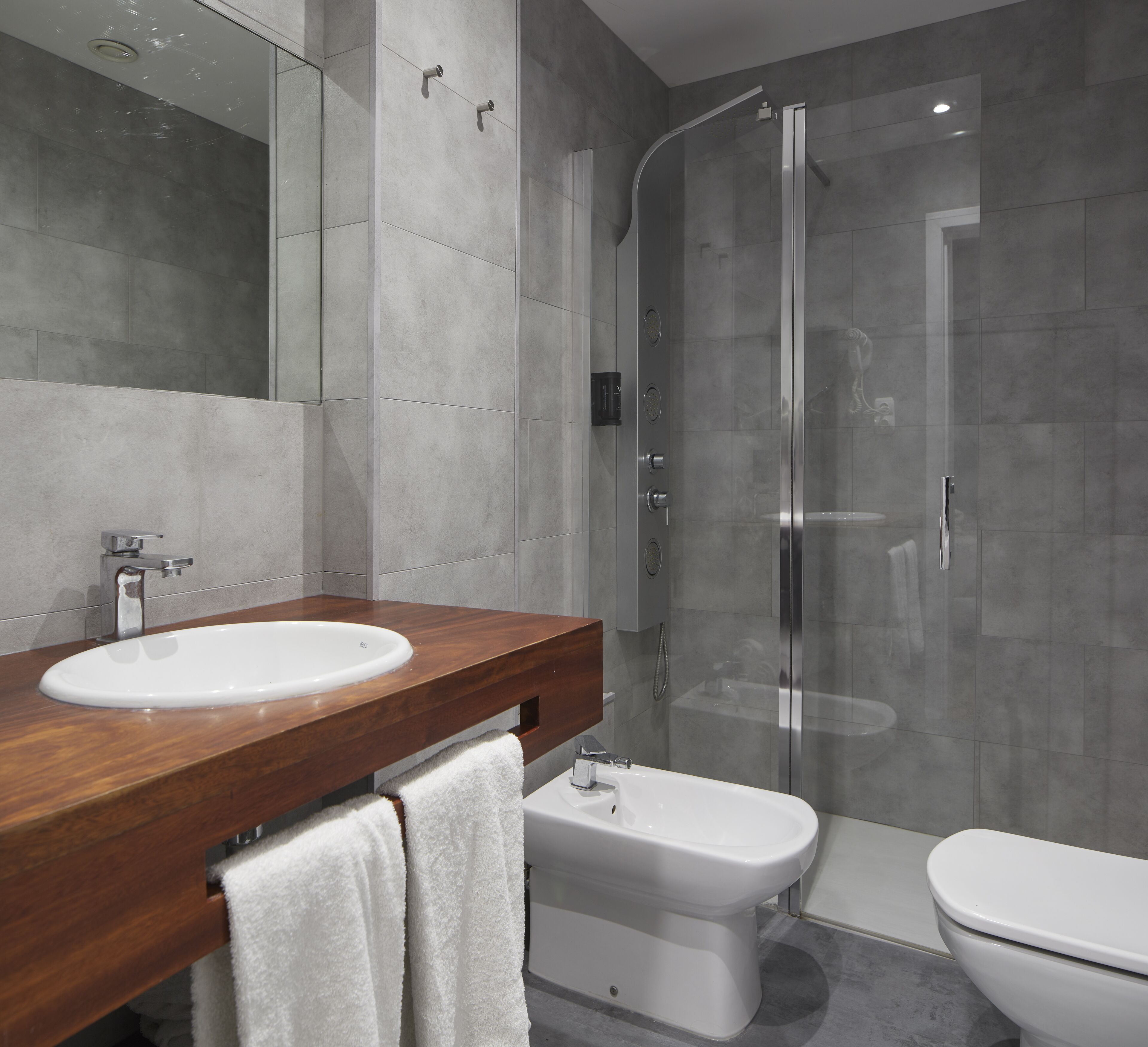 Une salle de bain moderne avec un meuble-lavabo en bois, un lavabo blanc, un bidet, des toilettes et une douche à parois de verre.