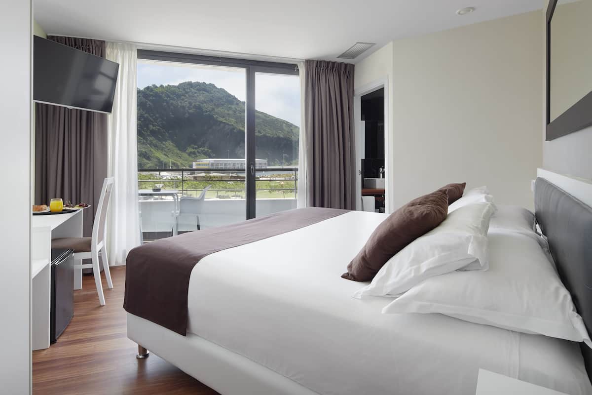 Una habitación de hotel moderna con una cama grande, un escritorio con una silla y un balcón con vistas a la montaña.