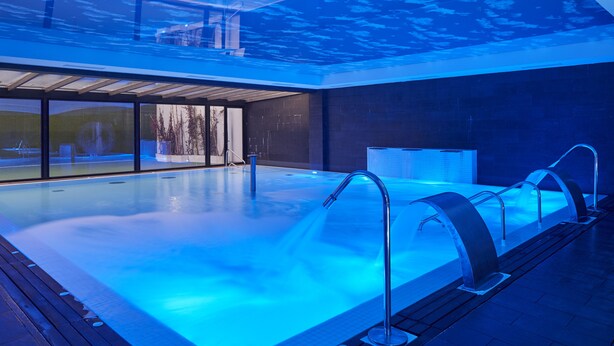 Una piscina interior de diseño moderno, con una pared de cristal y un techo que imita la superficie del agua.