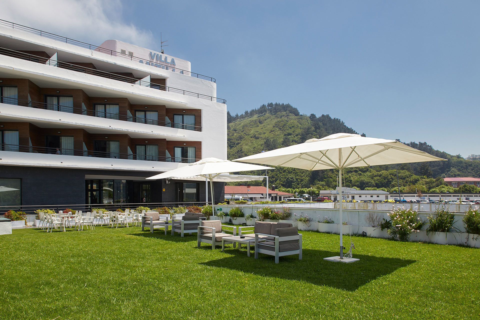 A hotel with outdoor seating, a white building, and a view of a hill.