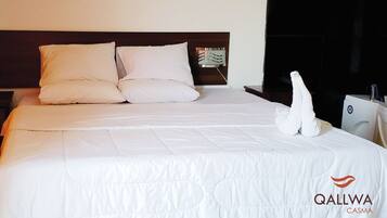 Una cama bien hecha con sábanas y almohadas blancas, un cabecero con un espejo decorativo y una toalla sobre la cama.