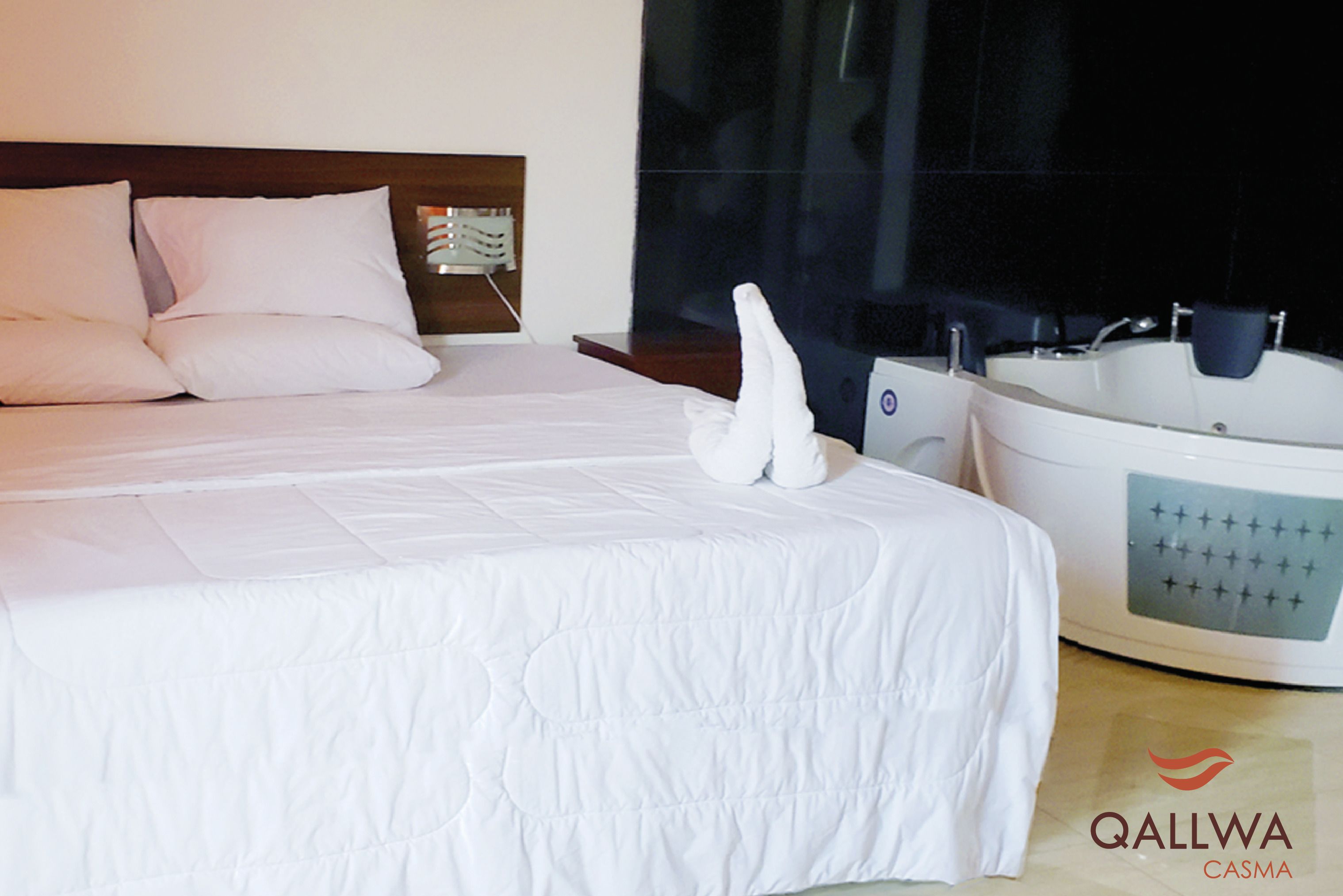 Una habitación de hotel con cama, almohadas, una bañera blanca y un logotipo visible.