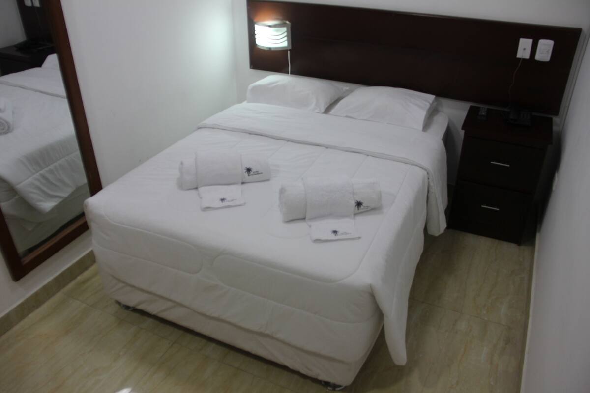 A hotel room with a large bed, a bedside table, a nightstand, and a mirror.