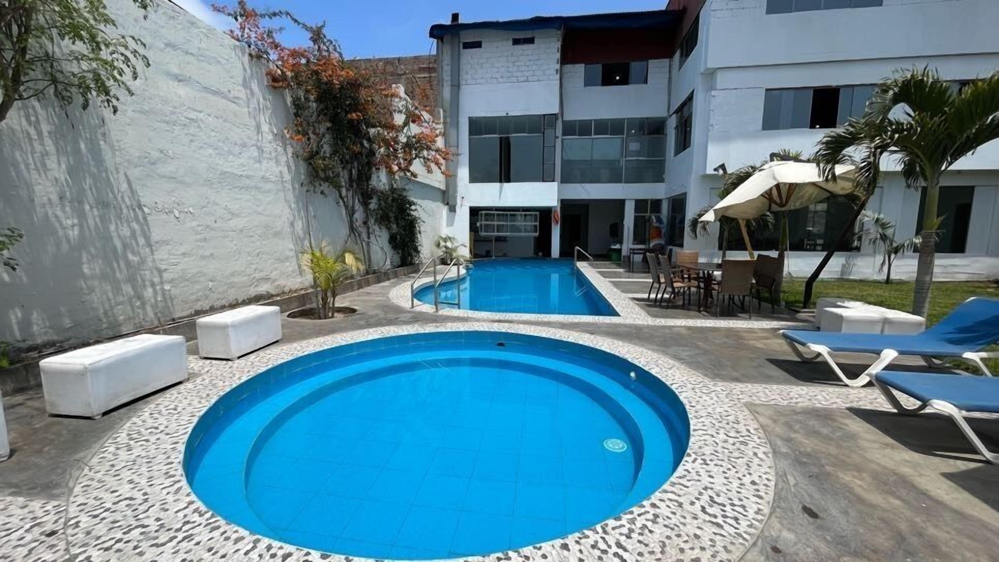 Una piscina con dos zonas separadas, rodeada por un muro blanco y un edificio moderno.