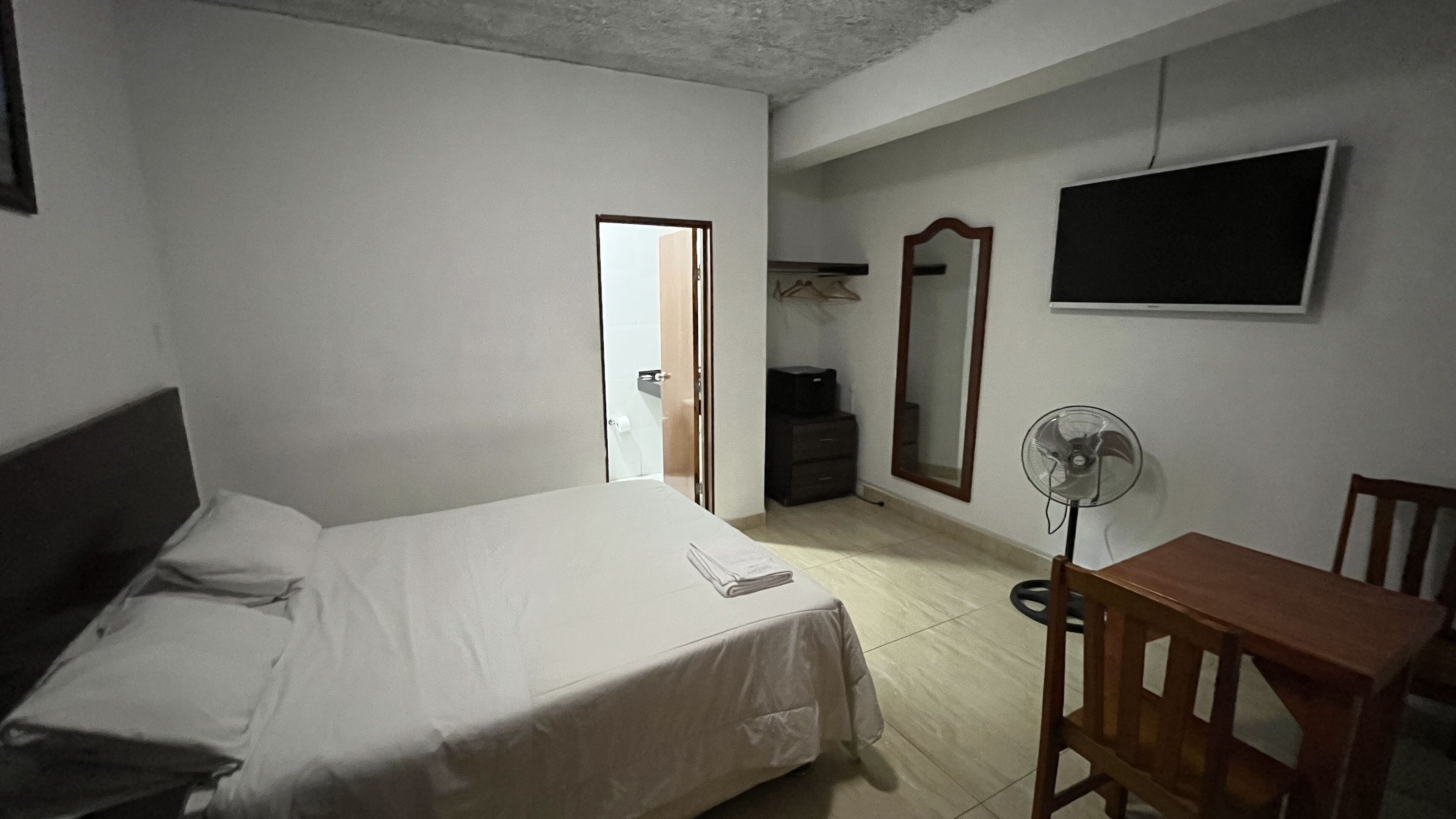 A bedroom with a bed, a desk, a chair, a mirror, and a television.