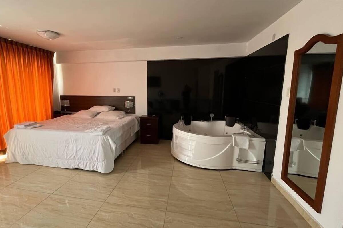 A modern hotel room with a large bed, a separate bathroom with a bathtub, and a large mirror.