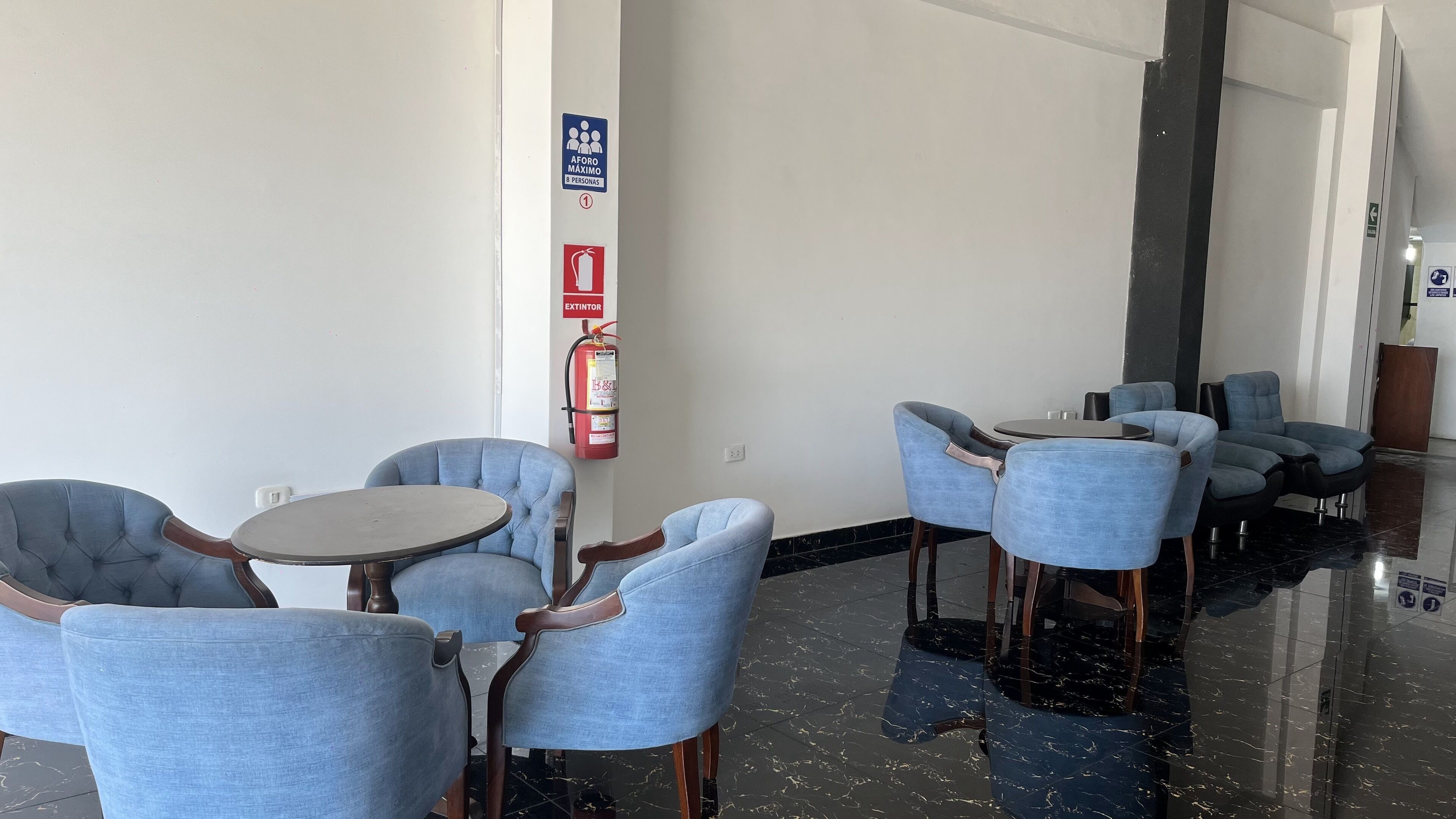 Un hall d’entrée avec des sièges, un extincteur et un panneau indiquant une capacité maximale de 8 personnes.