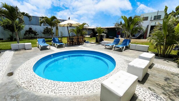 Une piscine circulaire aux carreaux bleus, entourée de chaises longues blanches et de jardinières blanches.