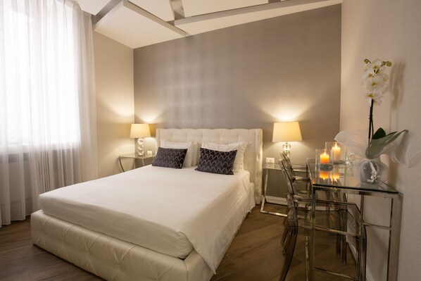 A modern hotel room with a large bed, two bedside lamps, a glass table with candles, and a clear chair. - Spagna Boutique (Rome)