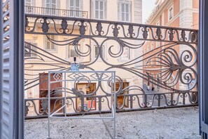 A balcony with ornate metal railings, a small table with a bottle, and a building with balconies in the background. - Spagna Boutique (Rome)
