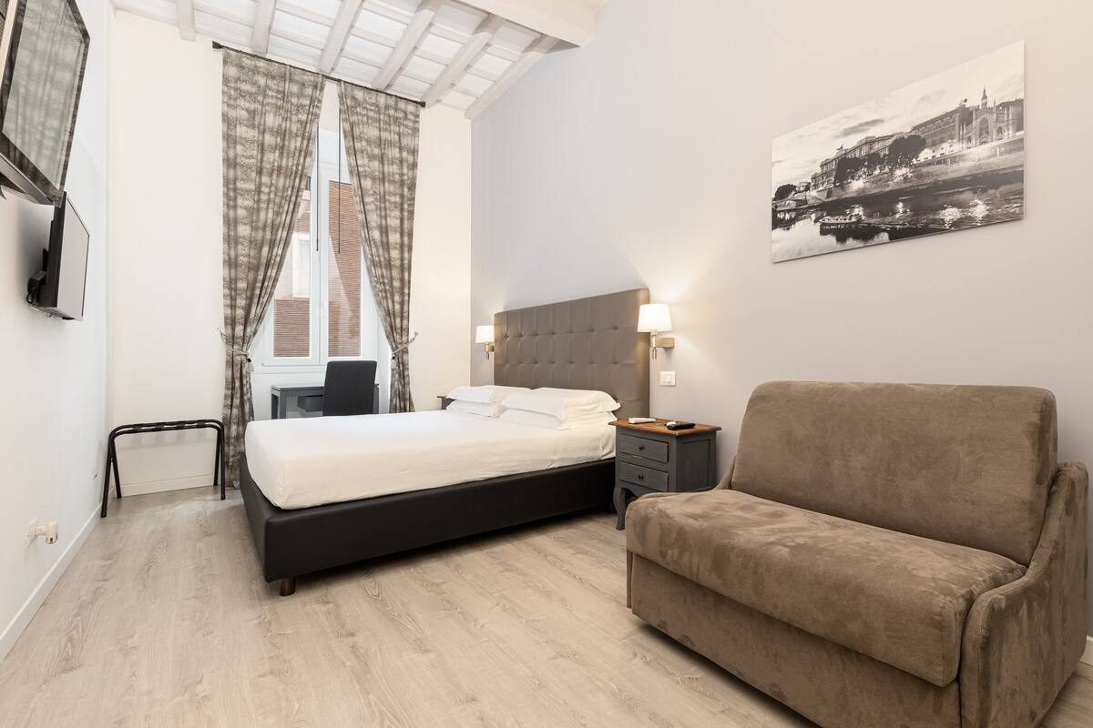 A bedroom with a bed, a sofa, a TV, and a painting on the wall.