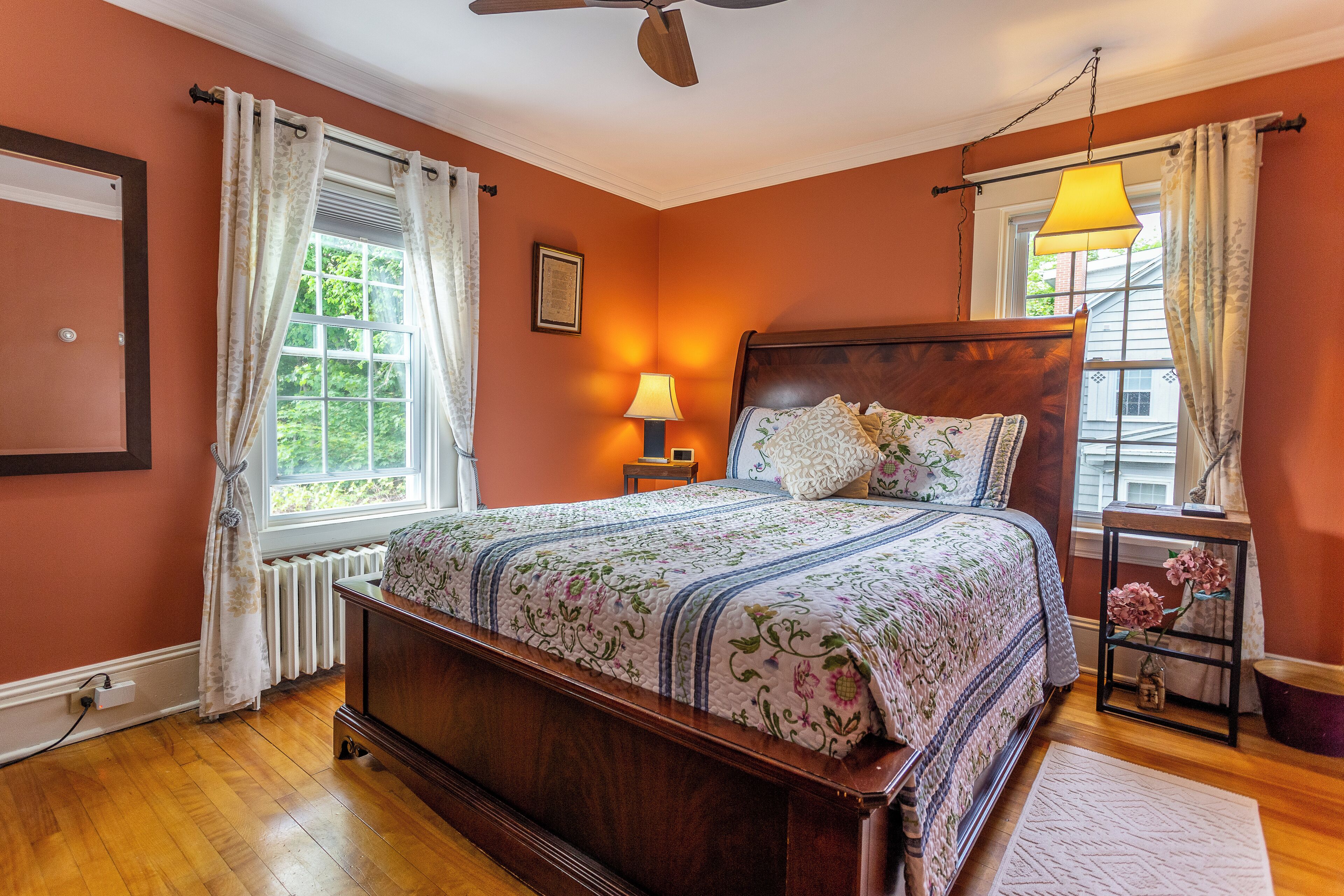 Un dormitorio con una cama de madera, una mesita de noche con lámpara, una ventana con cortinas y vista a la vegetación.