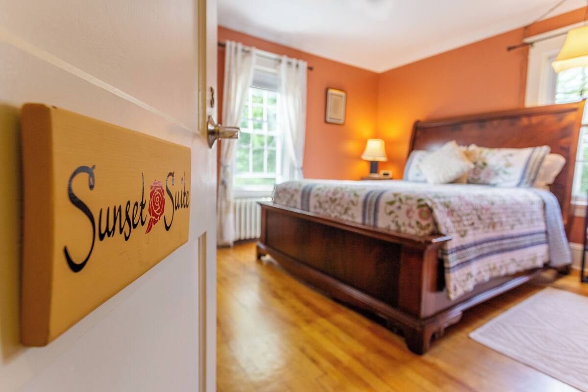 A bedroom with a wooden bed, a nightstand, a lamp, and a window with curtains.
