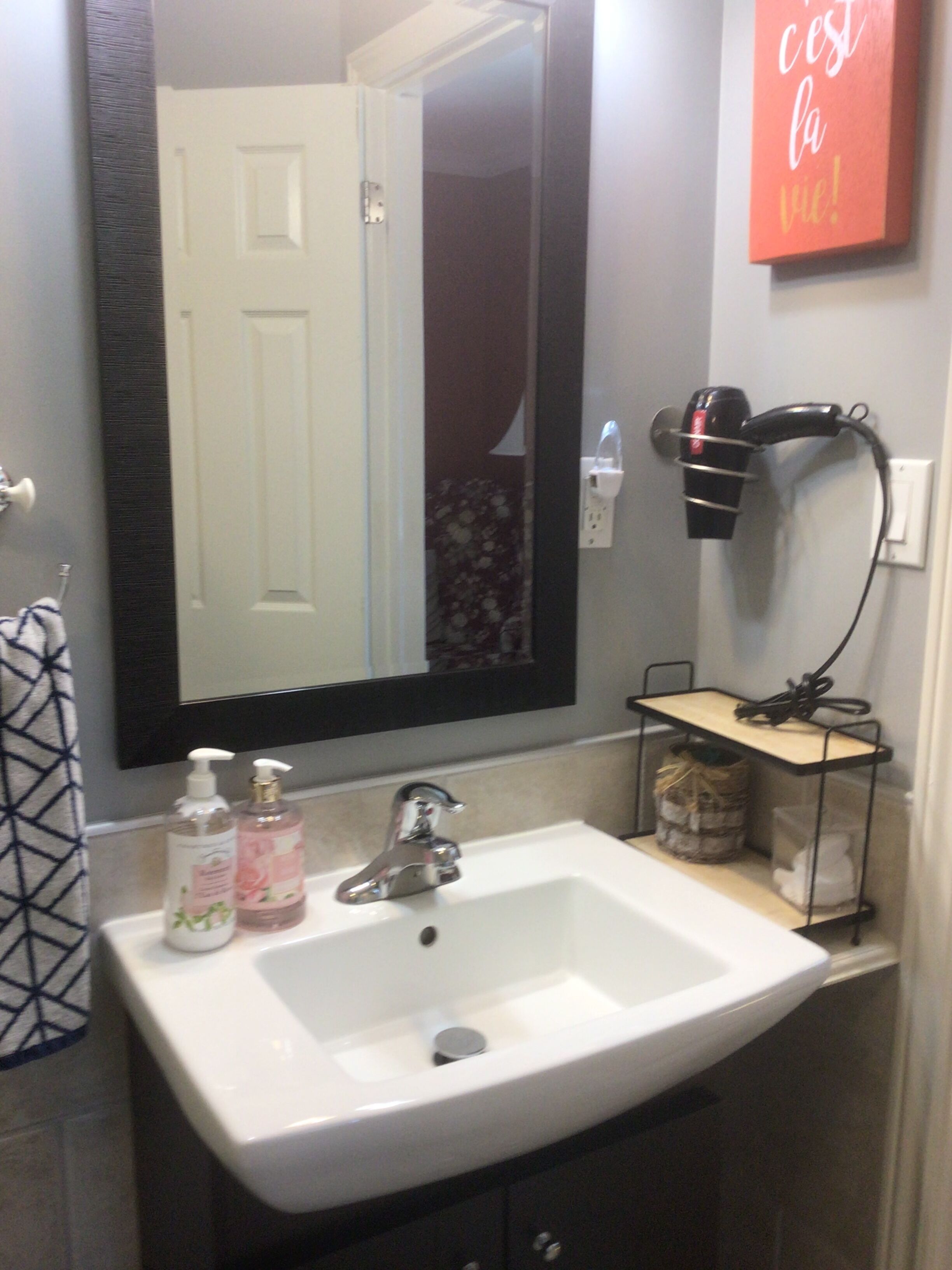 A bathroom with a white sink, a mirror, a hairdryer, and a shelf with toiletries.