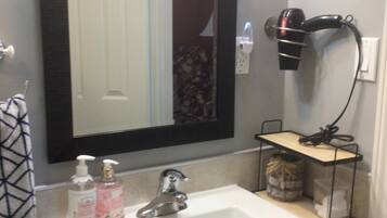 A bathroom with a white sink, a mirror, a hairdryer, and a shelf with toiletries.