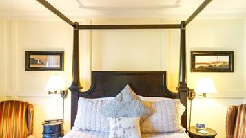 Un lit à baldaquin avec une couvre-lit matelassé et de nombreux oreillers, flanqué de deux tables de chevet avec des lampes, dans une pièce dont les murs sont ornés de tableaux encadrés.