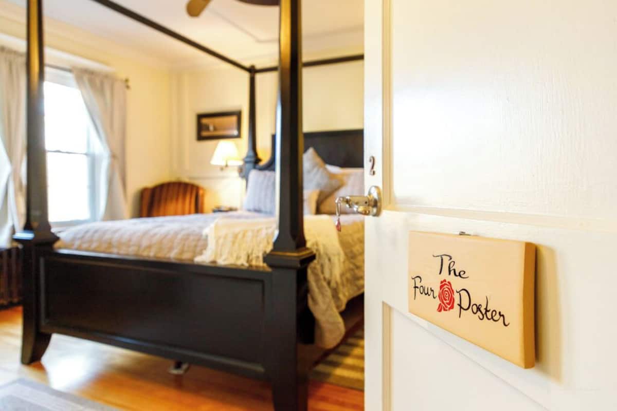 A four-poster bed in a hotel room with a sign on the wall reading "The Four Poster."