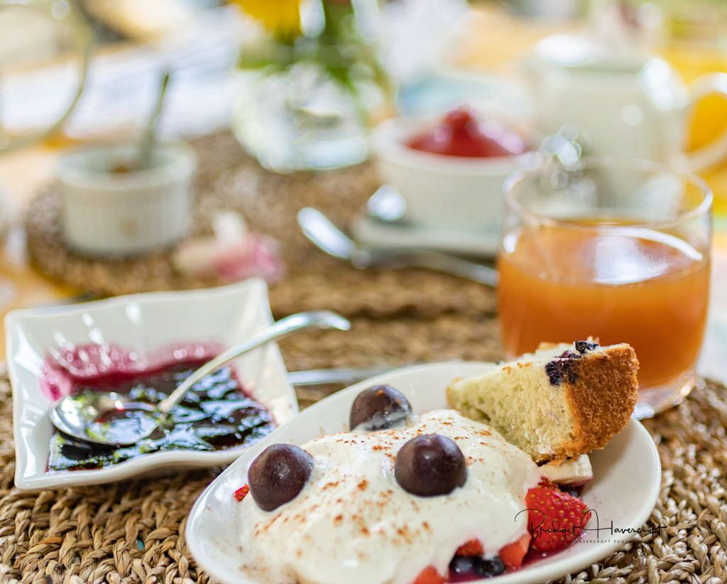 A breakfast setting with a plate of pancakes topped with berries and whipped cream, a glass of orange juice, and a small bowl of jam.