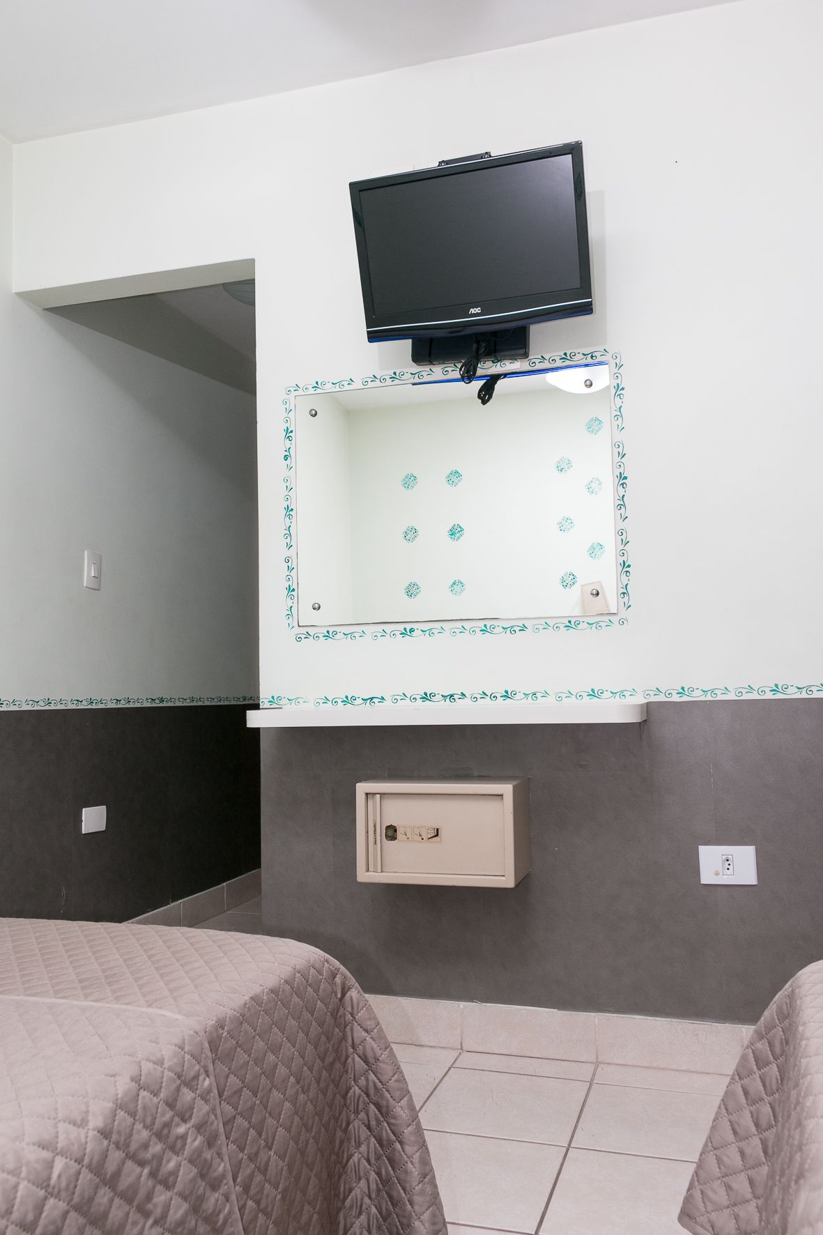 A hotel room with a television mounted on the wall, a small cabinet below it, and two beds with quilted covers.