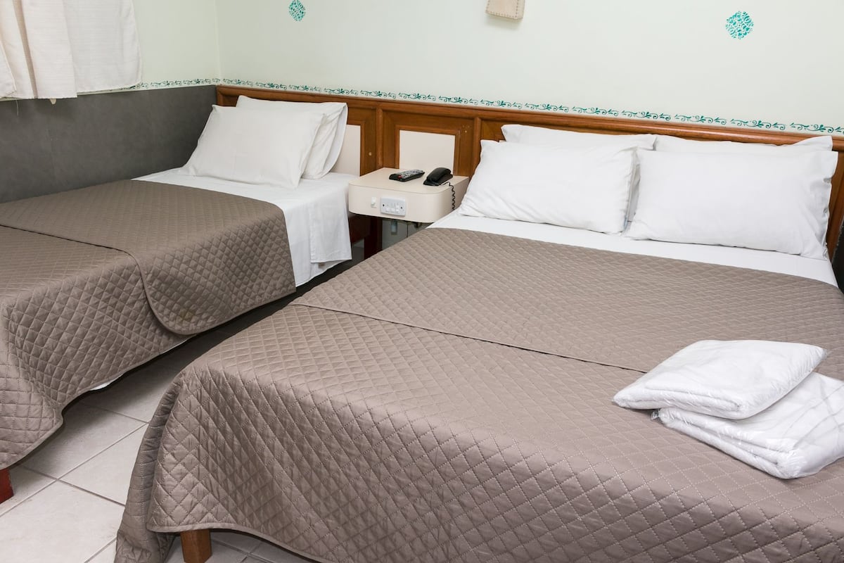 Two single beds with beige quilts, white pillows, and a nightstand with a phone and remote control.