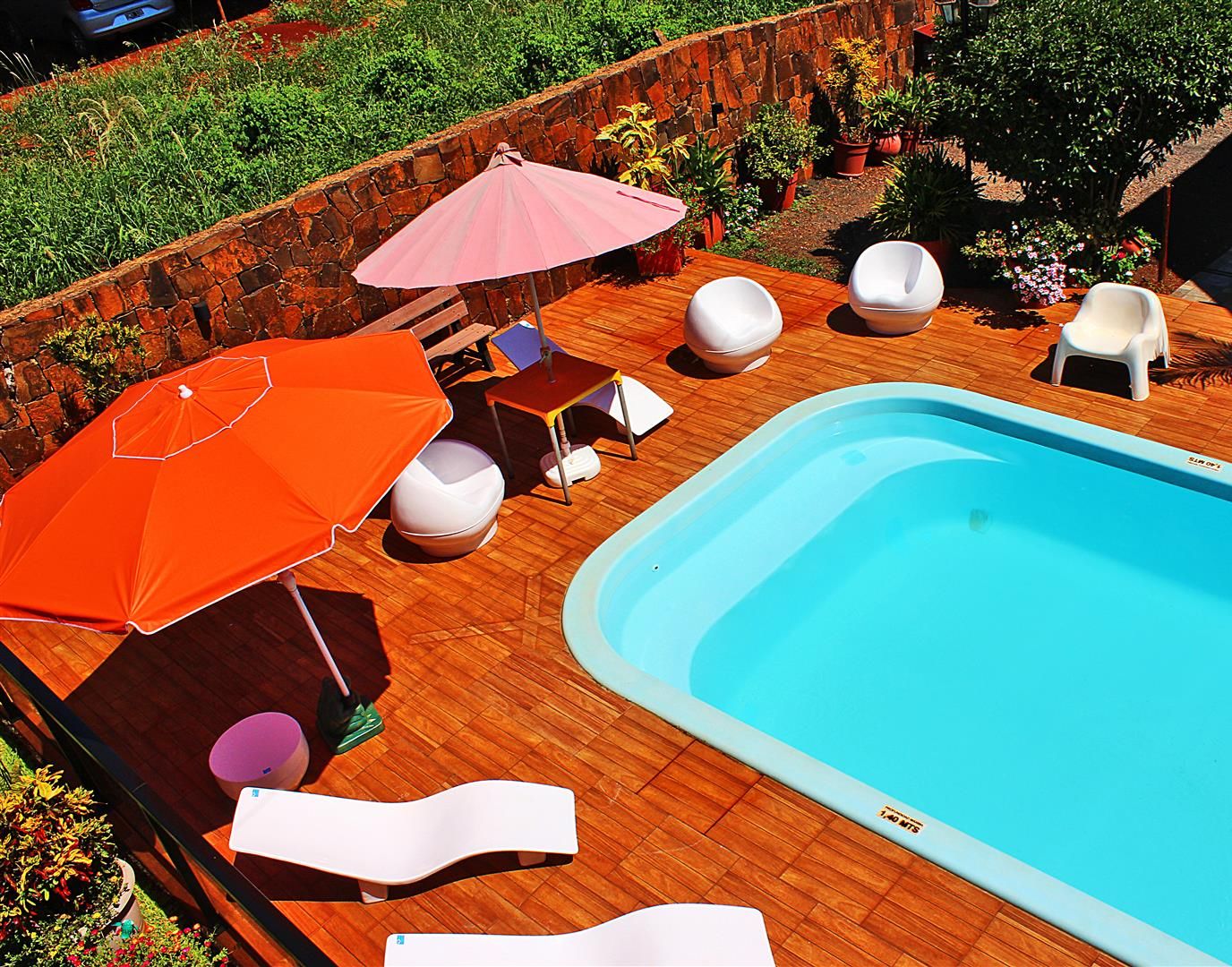 Una piscina con sillas de descanso y sombrillas, rodeada de una terraza de madera y plantas en macetas.