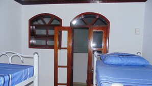 A room with two beds, a wooden door, and a window. - Hostel Praia Brava (Arraial do Cabo)