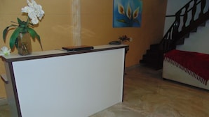 A reception desk with a vase of white flowers, a painting on the wall, and a staircase in the background. - Hostel Praia Brava (Arraial do Cabo)