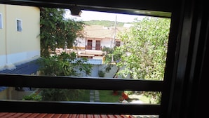 A view through a window with a tiled floor, a building with a tiled roof, and greenery. - Hostel Praia Brava (Arraial do Cabo)