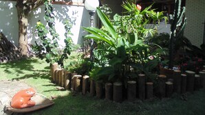 A garden with a variety of plants, a wooden fence, and a decorative frog statue. - Hostel Praia Brava (Arraial do Cabo)