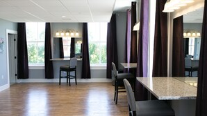A spacious room with a wooden floor, a large window with curtains, a dining table with chairs, and a mirror.